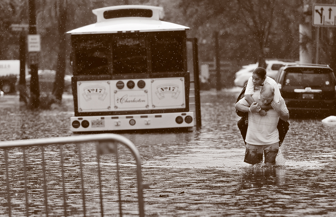 A man holds another person on his back through a flooded street.