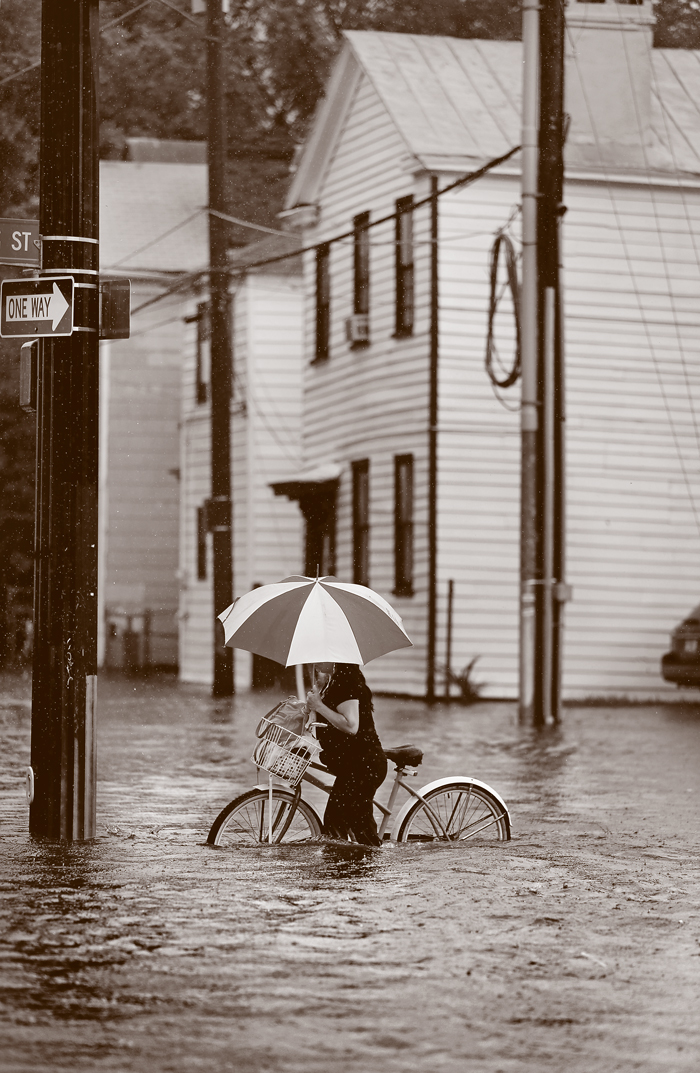 A biker with an umbrella pushes through high water.
