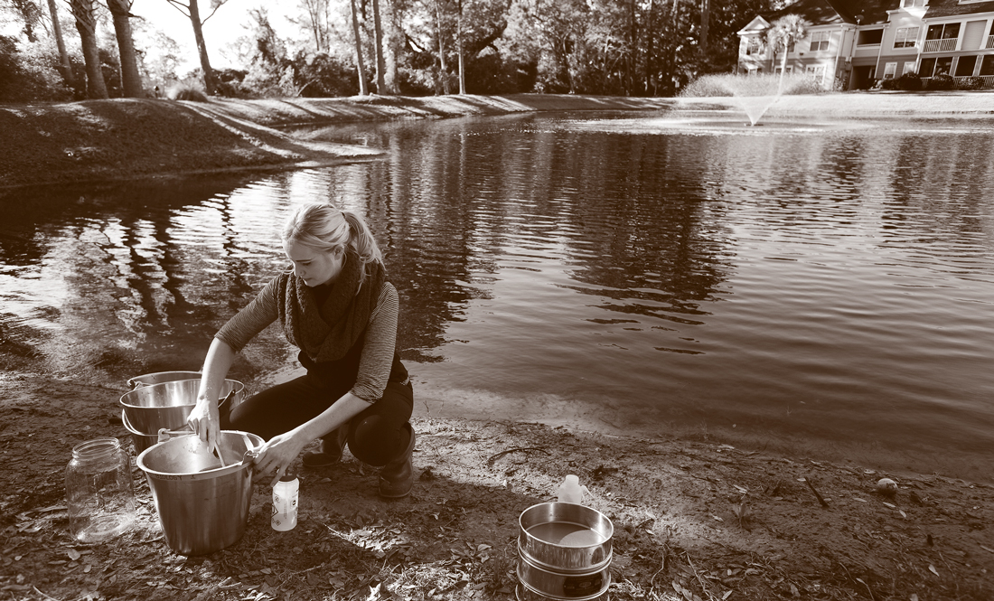 A woman performs tests in front of a stormwater pond.