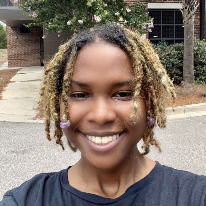 A smiling young Black woman with blonde dreadlocks.