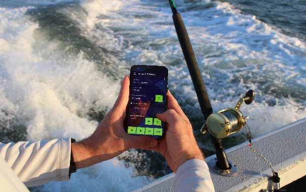Hands holding a mobile phone with the edge of a fishing boat and water visible.