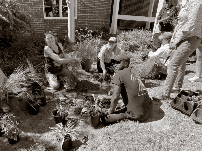 A group of young people sitting on the ground among potted plants.