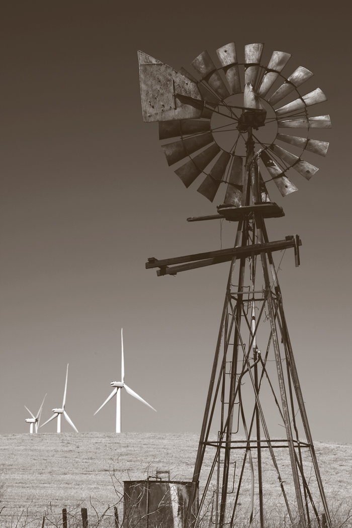 An oldfashioned farm windmill with modern turbines in the background.